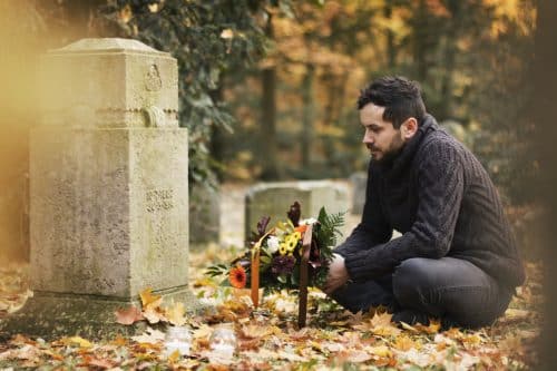 An adult man kneels down in front of the grave of a loved one that he lost due to a wrongful death in Alabama.