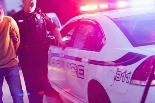 A police officer leading a drunk driver to his squad car.