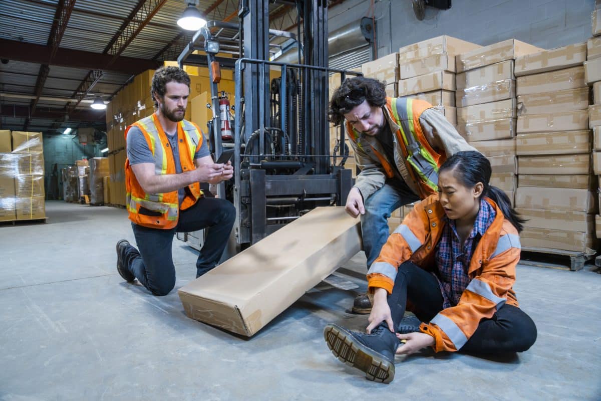 An injured warehouse worker holding her ankle in pain