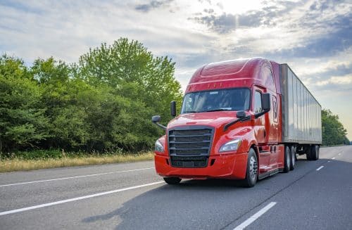 A semi-truck drives down the highway on a partially cloudy day.