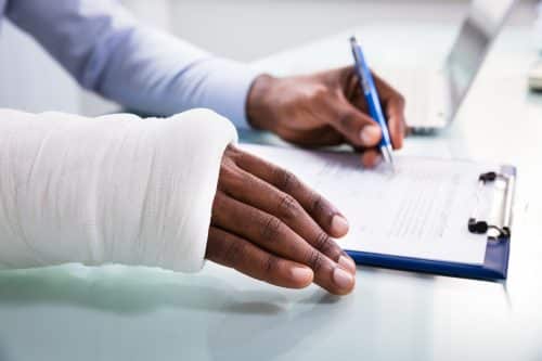 A person with one arm in a cast signs their medical documents.