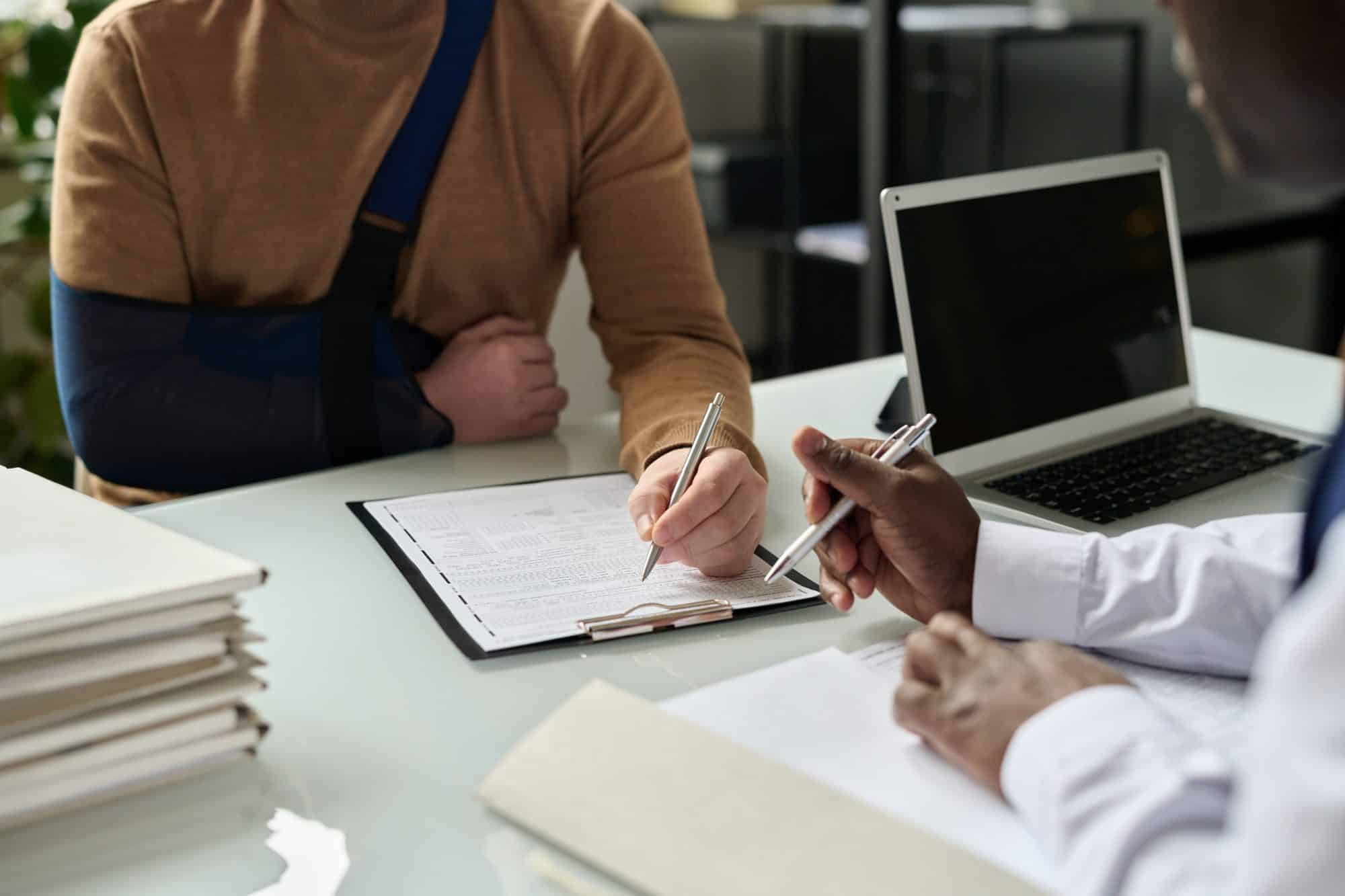 Plaintiff with their arm in a sling sitting at a desk with their semi-truck accident lawyer, filing an injury claim together